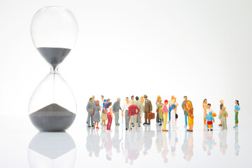 miniature people. group of different people stand near an hourglass against a white background....
