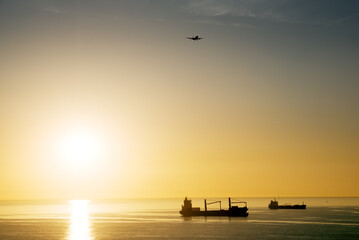 Sun rising above sea, distant ships and airplane