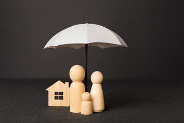 Wooden family figures under umbrella on concrete background.Insurance coverage concept.