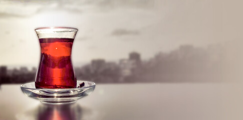 Turkish tea in glass in shape of Armudu stands on table against background of nature in contour light of sun, copy space, banner.