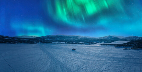 Scenic aerial night skies panorama on frozen lake, mountains with snow mobile traces, northern green lights. Scandinavian night winter landscape, Norway, Sweden
