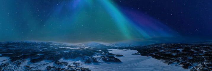 Very wide scenic aerial panorama on frozen lake, mountains with snow mobile traces, northern green lights over mountains. Scandinavian night winter landscape, Norway, Sweden