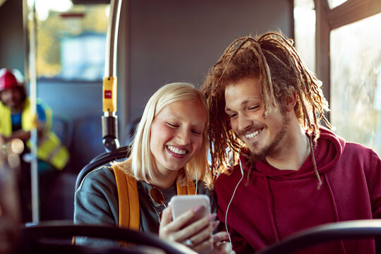 Smiling young couple sitting on bus looking at smartphone