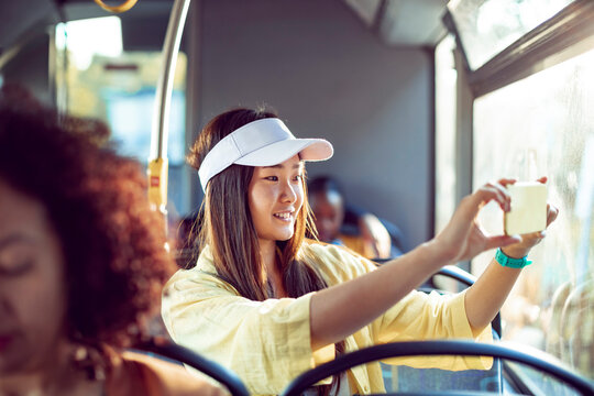 Young woman sitting on bus taking picture out window