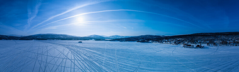 Very wide scenic close up panorama on frozen lake, mountains with snow mobile traces, sunny blue...