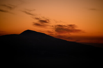Dark silhouette of mountain with bright orange sunset sky on background