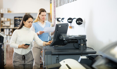Women working in publishing facility, using printer, pushing buttons on display.