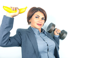 Happy beautiful business woman in a suit lifts a dumbbell and a banana in her hands. Fitness and health. Proper nutrition and excellent results.