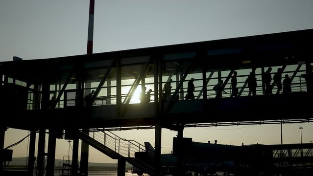 Passengers boarding using an air bridge. People walk in silhouette along ramp. Passengers boarding to airplane in airport