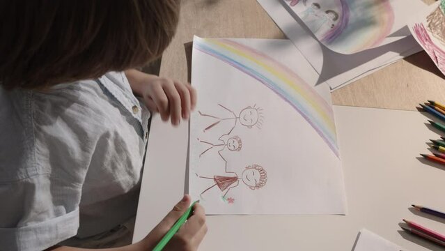Young boy brings his family to life on paper through his drawing skills. The artwork portrays a cozy family idyll, child's creativity and imagination. Loving and joyful family. Divorce and children