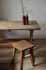 Minimalist realistic composition. Fragments of an old country house interior design - plastered lighted walls, clay glazed bottles, plant branches, very shabby wooden table and chair 