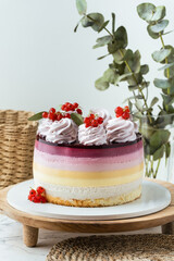 Summer cake with different mousse berry layers decorated with red currant and whipped cream on the wooden cake stand.