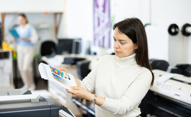 Female employee of the copy center checks the quality of the print on the color chart