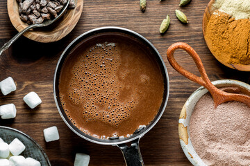 A look into a small pot of freshly made hot cocoa with ingredients all around.