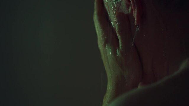 In a gloomy setting, a man relaxes under a warm shower, letting the water run down his bare skin. His tired body regains strength and he thinks about the importance of taking care of his skin