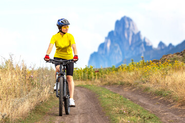 beautiful woman cyclist in a yellow shirt rides a bicycle along a field road. sports, hobbies and entertainment for health