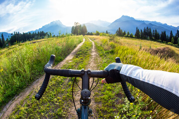 hands on the handlebars of a bicycle of a cyclist riding along a trail in nature. Point of view