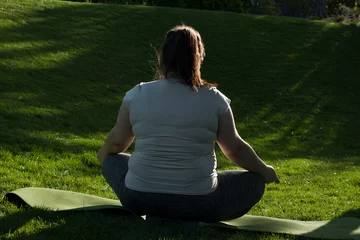 Poster Portrait of overweight Caucasian middle-aged woman practicing yoga in nature. Fat woman meditating, relaxing in lotus position, sitting on fitness mat. Calm, relaxed, zen, stop stress. View from back © lilu2005