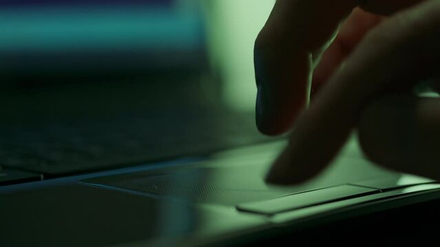 Under dim lighting, a hacker programmer is intently busy at his laptop, using a touch-sensitive mouse and keyboard. Close-up of a programmer's hands working pressing laptop keyboard buttons