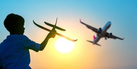 Silhouette of a boy launches a model airplane into the sky against the backdrop of the setting sun....