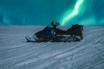 Close up photo on snow mobile standing at snow slope at night with with night northern green lights...