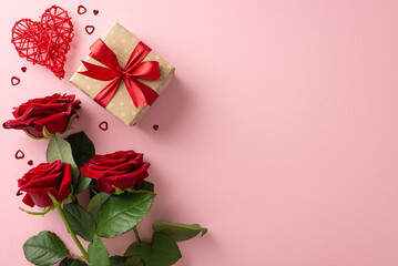 Express your love this Valentine's Day with top view craft paper gift box, rattan heart, red roses, festive confetti on a pastel pink backdrop, ideal for your message or advert