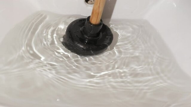 Eliminate the blockage with plunger. A housewife hands try to eliminate the block with a plunger in the kitchen.