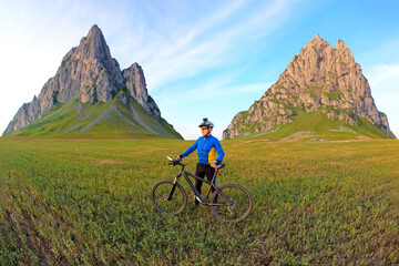 cyclist with a bicycle is resting on a green field against a blue sky. sports and recreation in...