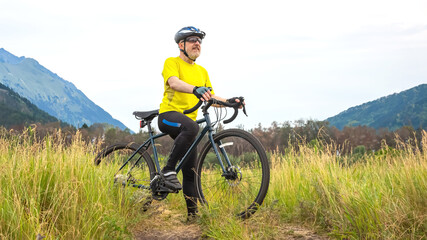 bearded man cyclist in yellow clothes is resting on a bicycle on the road in nature. sports, hobbies and entertainment for health