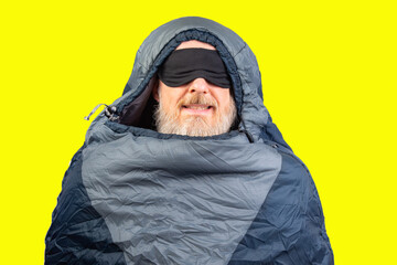 bearded man in a sleeping bag on a yellow background. equipment for recreation in tourism and travel