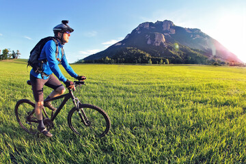Fototapeta premium cyclist rides a bicycle on the green field towards the sun