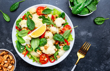 Healthy fresh vegan salad of cauliflower, baked paprika, cherry tomatoes and spinach with walnuts, dark table background, top view