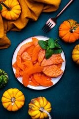 Baked pumpkin slices caramelized in orange glaze, autumn or winter dessert food on dark green table background. Top view