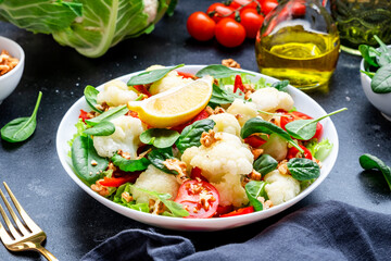 Healthy fresh vegan salad of cauliflower, baked paprika, cherry tomatoes and spinach with walnuts, dark table background, top view