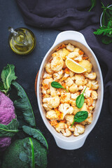 Baked cauliflower in garlic lemon dressing with olive oil in baking dish, dark background, top view