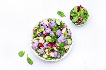 Healthy fresh salad from purple cauliflower, grilled chicken breast, cucumbers, red onion, radicchio, spinach with pumpkin seeds, white table background, top view