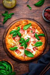 Homemade pizza with pancetta, mozzarella cheese, spicy sauce and green basil leaves on old wooden table background, top view