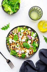 Tasty fresh salad with grilled zucchini, feta cheese, walnuts, red onion and spinach on white table background, top view