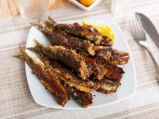 Grilled on fire sardines served with slice of lemon on white plate, traditional andalusian dish