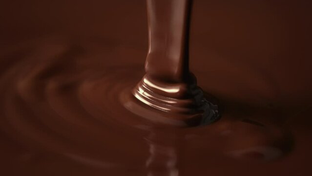 Slow motion shot pouring melted chocolate, close-up seamless dripping hot liquid chocolate flows, waves flowing molten chocolate or dark caramel sauce. Chocolate wavy drip. Confectionery cooking
