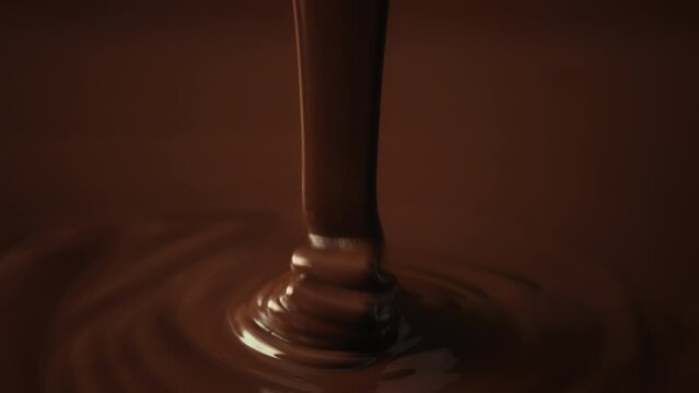 Slow motion shot pouring melted chocolate, close-up seamless dripping hot liquid chocolate flows, waves flowing molten chocolate or dark caramel sauce. Chocolate wavy drip. Confectionery cooking