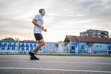 adult caucasian man jogging on the running track male athlete in stadium training run in sunny spring or summer day real people healthy lifestyle concept