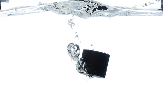 Black Cosmetic container fall into clear water with air bubble. Cosmetic treatment container drop to clear water of freshness. White background isolated freeze element