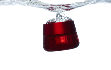 Red Cosmetic container fall into clear water with air bubble. Cosmetic treatment container drop to clear water of freshness. White background isolated freeze element