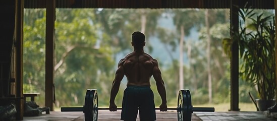 Man exercising with barbell. Male bodybuilder doing weight training in the gym, view from behind. - obrazy, fototapety, plakaty