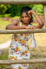 A portrait of a young african woman leaning against a wooden support at a park