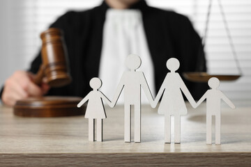 Family law. Judge with gavel sitting at wooden table, focus on figure of parents and children