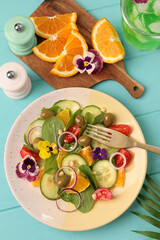 Delicious salad with orange, spinach, olives and vegetables served on turquoise wooden table, flat lay