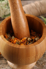 Mortar with pestle and calendula flowers on wooden table, closeup. Medicinal herbs