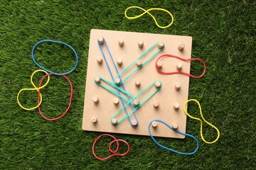 Wooden geoboard with rubber bands on artificial grass, flat lay. Educational toy for motor skills...